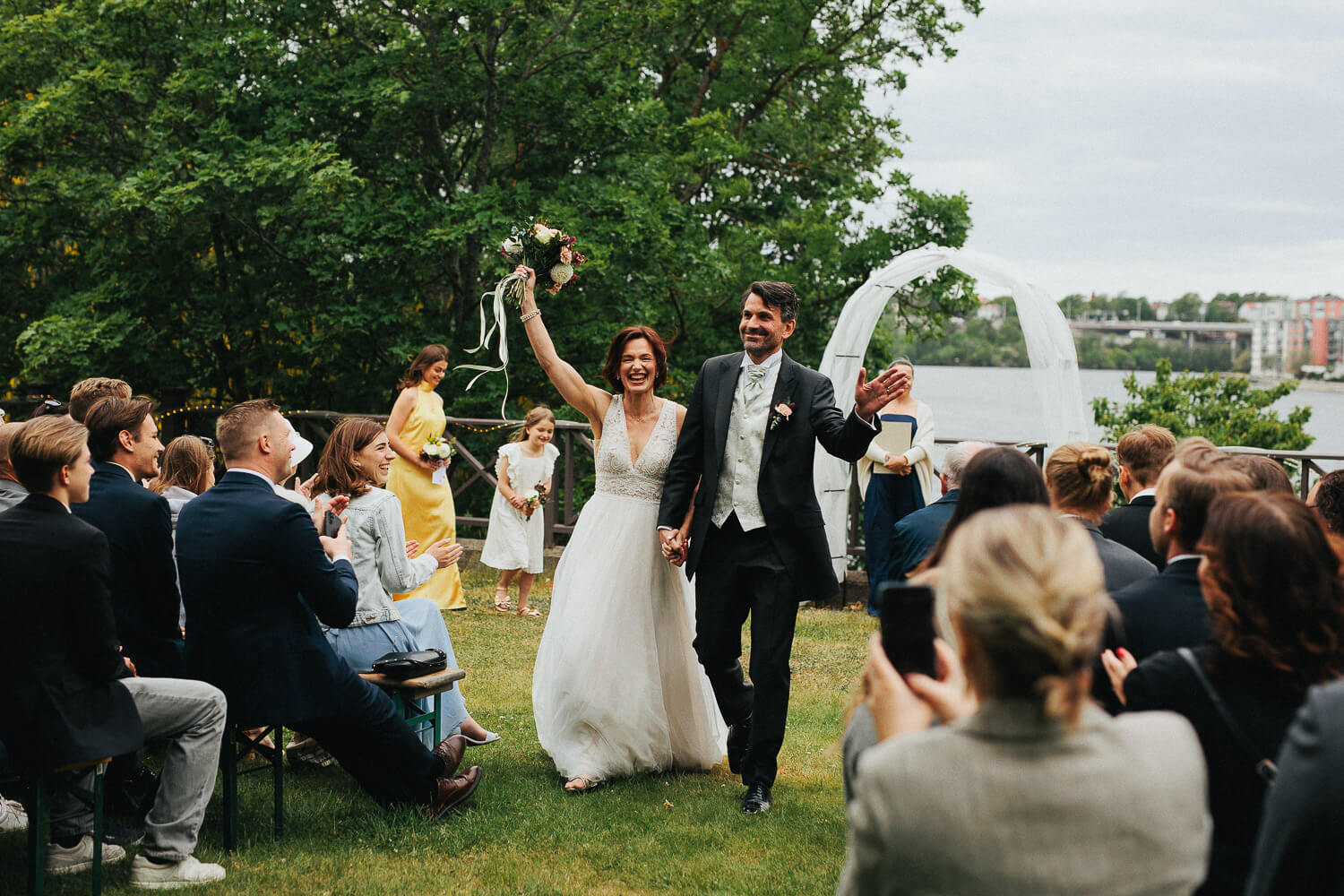 Elin och Love firar vigseln med armarna i luften när de går ut genom ceremonigången på Carlshälls Gård.